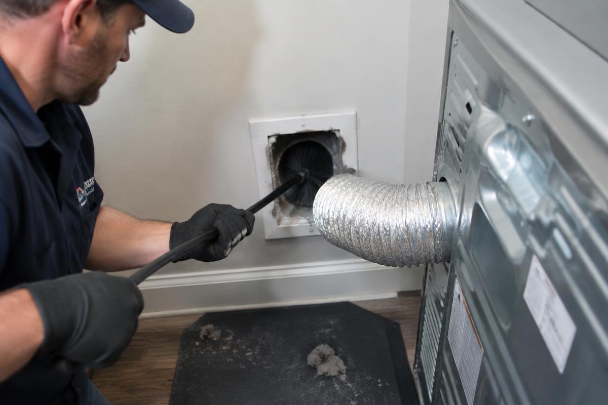 Representative photo: a technician cleaning lint from a dryer vent line with a rotary brush